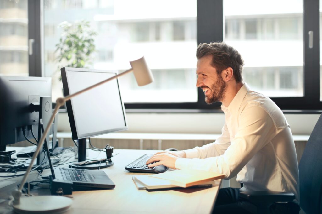 man sitting at desk, looking at computer, smiling